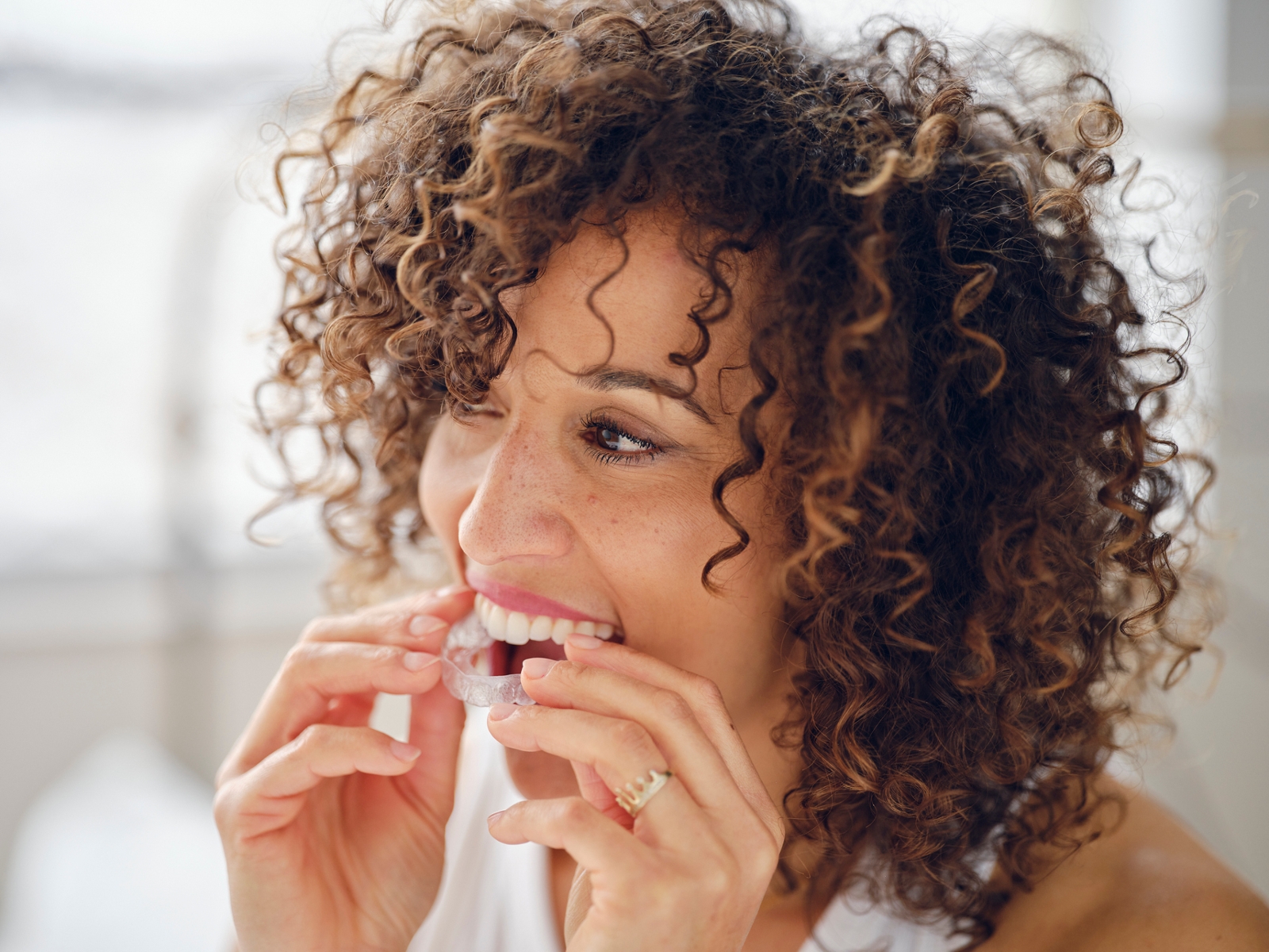 Woman placing a clear aligner over her teeth for Invisalign treatment