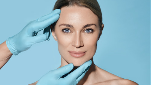 Gloved hands gently assessing a woman's facial symmetry and harmony during a dental evaluation.